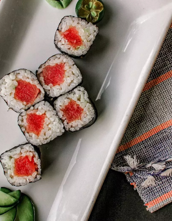 Plateau de sushi rolls variés avec saumon, avocat et garnitures dressés sur une assiette noire