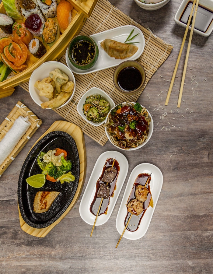Vue de dessus sur un assortiment de plats japonais avec sushis, brochettes, légumes, sauces et accompagnements
