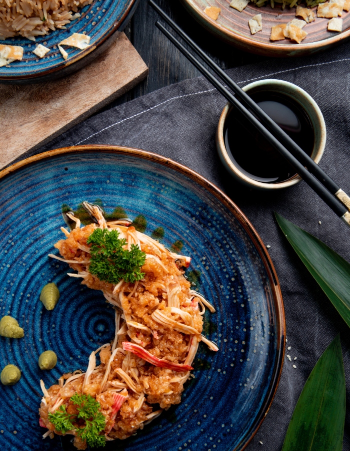 Plat japonais croustillant servi dans une assiette bleue avec sauce soja, baguettes et décoration végétale